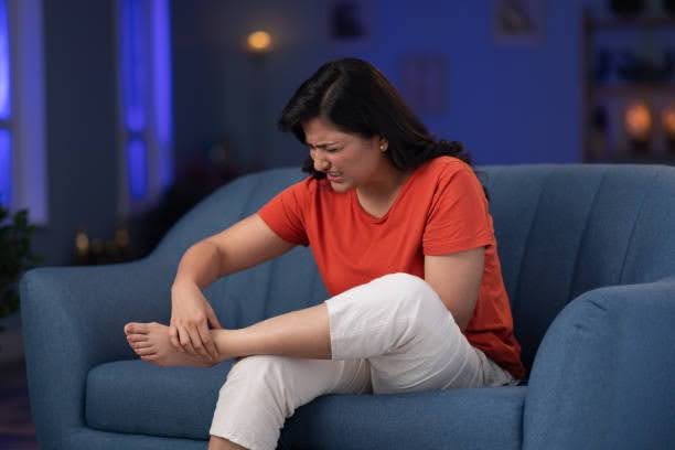 Woman sitting on a couch holding her ankle in pain